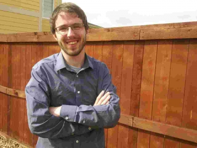Dominic Smith, licensed professional counselor, registered play therapist, outdoors, smiling, standing next to a wooden fence with arms crossed
