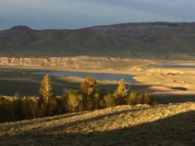 Landscape photo looking out across some grasslands, trees, a lake, and hills