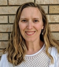 April Malcolm, licensed marriage and family therapist, smiling, outdoors standing next to a brick wall