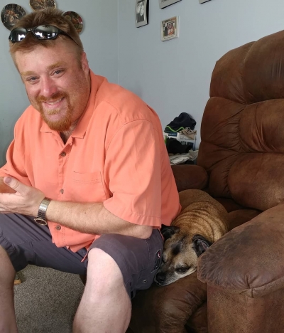 Nathan Preston, licensed marriage and family therapist, sitting in a chair with his therapy dog, Titus