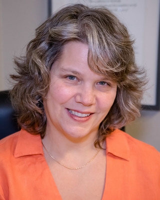 Angi Brown, registered psychotherapist, smiling, with shoulder length wavy hair and wearing an orange shirt
