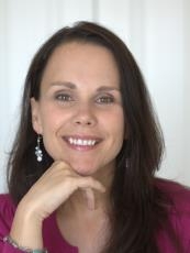 Shauna Fisher, licensed marriage and family therapist, smiling, wearing a cranberry-colored shirt and resting her chin on her hand.