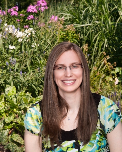 Laura Molzer, licensed marriage and family therapist, smiling, wearing glasses and a colorful top with greens, blues, black and white