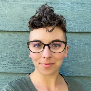 Stephanie Rayburn, marriage and family therapist candidate, with short, curly dark brown hair that is shaved on the sides, light skin, black-framed glasses, and a green shirt.