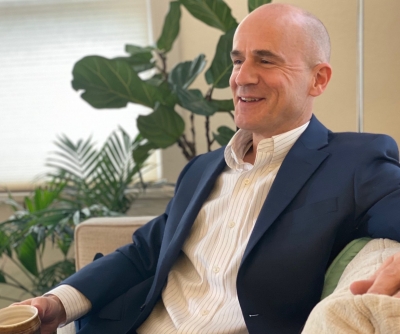 Joseph Librizzi, licensed clinical social worker, smiling, sitting on a sofa, wearing a white, button-up shirt and dark blue suit jacket