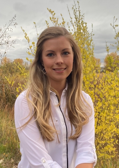 Aubrey Hahn, licensed professional counselor, smiling, wearing a white shirt, sitting near a bush with yellow leaves