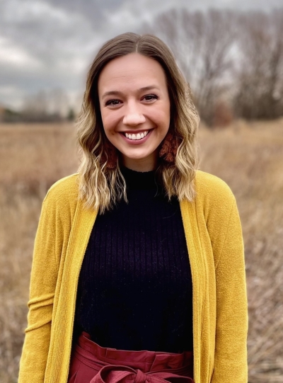 Anna Muller, candidata a terapeuta matrimonial y familiar, sonriendo, de pie al aire libre en un campo