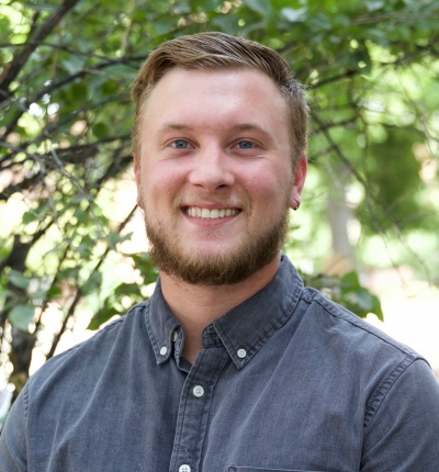 Evan Bostrom, licensed professional counselor, smiling, wearing a blue, button-up shirt, with trees in the background
