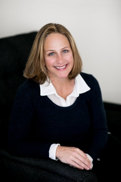 Tracy Heinz, licensed clinical psychologist, smiling, sitting in an office, with shoulder-length hair, and wearing a white shirt and a black sweater