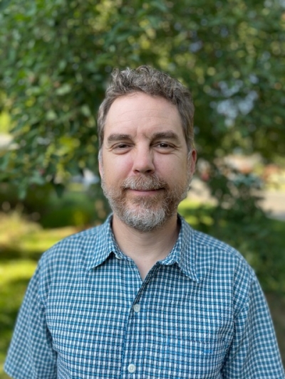 Dr. Trotter, licensed psychologist, standing outdoors near a tree, wearing a blue and white checkered, button up shirt