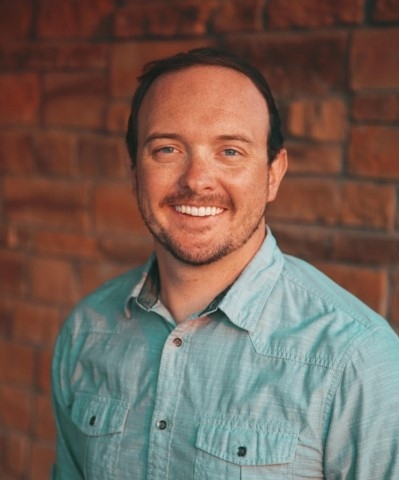 Keaton Brown, licensed marriage and family therapist, smiling, standing near a brick wall, wearing a light blue button up shirt