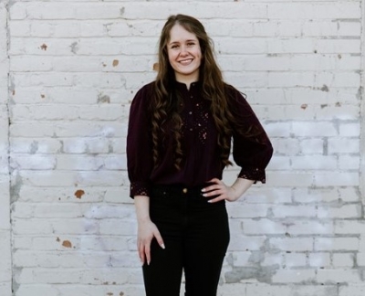 Rachel Weeks, licensed professional counselor candidate, smiling, wearing a black shirt and black pants standing in front of a white brick wall. 