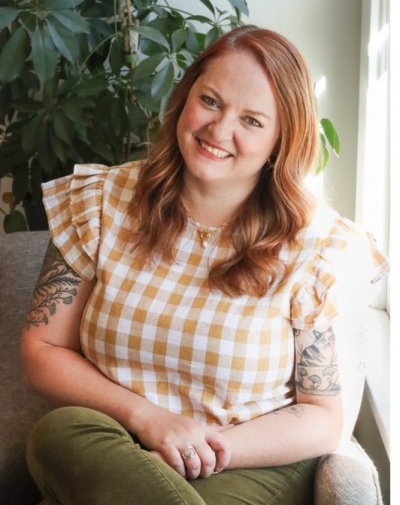 Jessie Charbonneau, licensed professional counselor, licensed addiction counselor, smiling, sitting in a chair wearing a tan and white checked shirt and olive green pants.