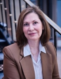 Kathleen McNamara, PhD, licensed psychologist, wearing a brown jacket and white shirt, sitting on a staircase