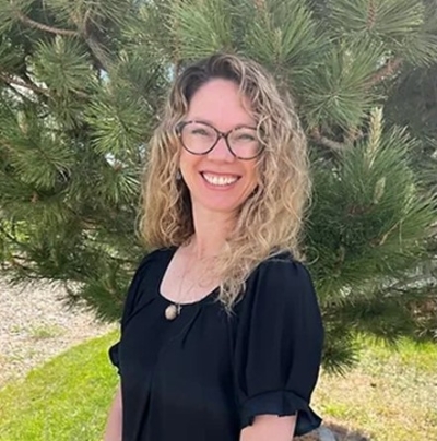 Shanna Tipton Green, licensed professional counselor, standing near an evergreen tree, smiling, wearing glasses and a black short-sleeved top.