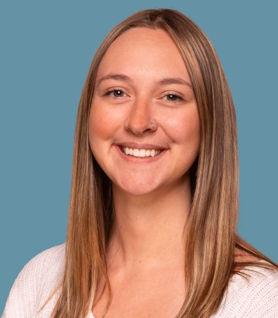 Mikinzie Hoffman, licensed professional counselor candidate, smiling, wearing a white sweater against a light blue background