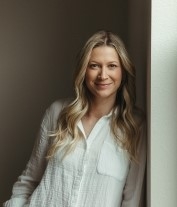 Maggie Knepp, licensed professional counselor, smiling, leaning against a wall, wearing a long-sleeved white shirt