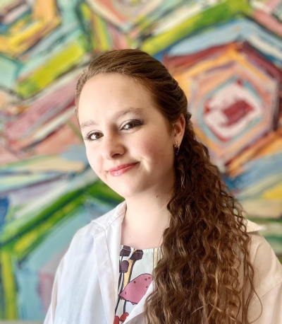 Rebecca Castle-Waller, licensed clinical social worker, smiling, wearing a colorful shirt with drawings on it and a white shirt over it, with a multi-colored wall in the background