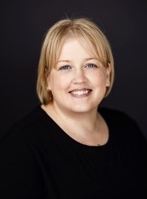 Roxann Shook, licensed professional counselor, smiling, wearing a black shirt against a dark background