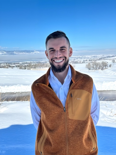 Nathan Daly, licensed clinical psychologist, smiling, wearing a white, button-up shirt and casual vest, standing outdoors, with snow in the background