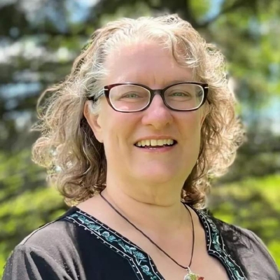 Heather Fisher, licensed professional counselor candidate, smiling, wearing glasses, with trees in the background