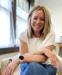Julie Kittredge, licensed professional counselor, smiling, wearing a white top and blue jeans, sitting and leaning forward toward the camera