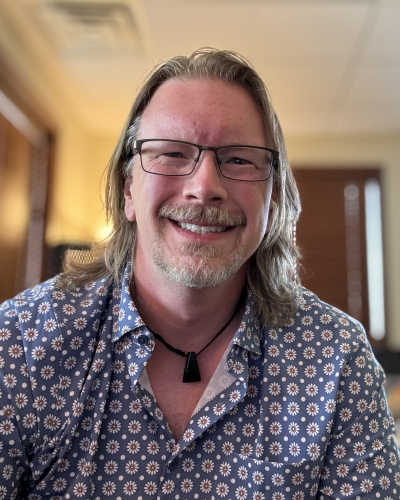 a 46 year old male with shoulder length hair and glasses wearing a button up shirt with a floral print