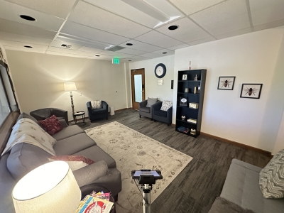 Waiting room with sofa and chairs, a bookcase, wooden floors, and a large area rug, 