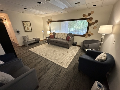 Waiting room with large window, sofa and chairs, wooden floor, and a large area rug