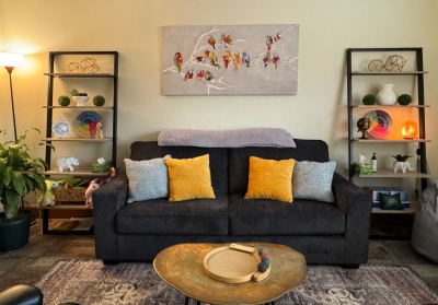 Office with sofa with colorful pillows, bookcases, a floor lamp, plants, and a small table