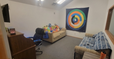 Office with sofas, a desk and chair, and colorful wall hanging.