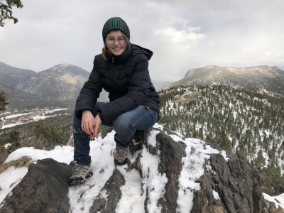 On a mountain, wearing a knit hat, jacket, and pants.