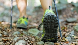 Imagen de una persona caminando en el bosque con bastones de senderismo. La imagen se amplía en los zapatos y la parte inferior de los postes.