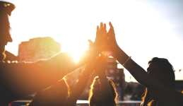 Group of people giving high fives with the sunrise above a cityscape in the background