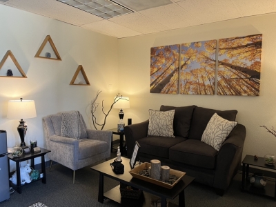 Office with chair and small sofa, lamps, and artwork on the wall.