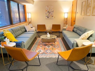 A group therapy room at Bloom Counseling and Nutrition with two light blue sofas, several chairs, set around a small coffee table and area rug