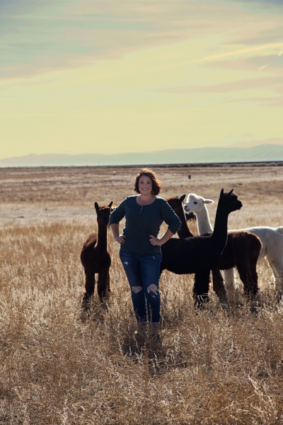 Christy Stiger standing in a field on her ranch with several alpacas