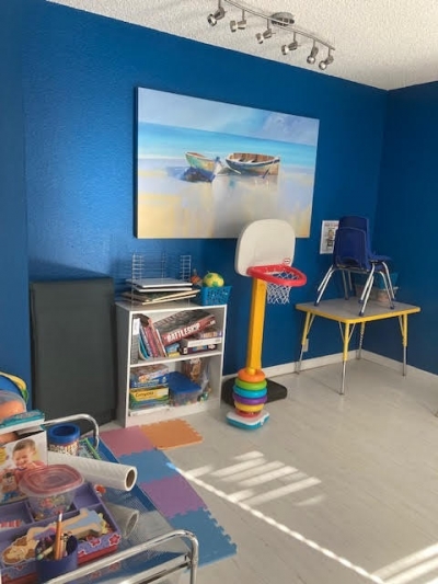 Room with blue walls with water and boat canvas painting, puzzles, table and chairs, mini basketball hoop
