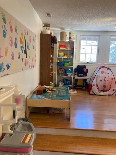 Play kitchen, canvas Array wall painting with many colors of handprints from clients, bookshelves with games, puzzles, and activities. Train table to play on. Windows to allow natural lighting. 