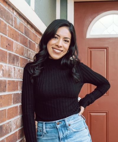 Erandi Herndon, licensed marriage and family therapist, smiling, standing outdoors, leaning against side of a building