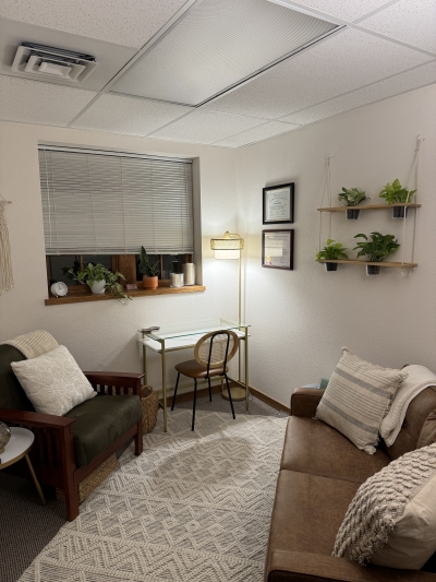 Therapy office with a chair and small sofa a floor lamp, several potted plants, and a window.