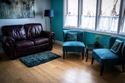 Therapy room with 2 chairs and a love seat, well-lit with large windows