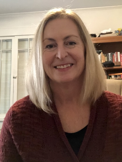 Sarah Murphy, smiling, wearing a rust colored sweater and black shirt, with a bookcase in the background