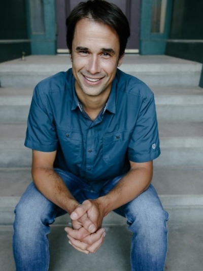Jonah Bryan, licensed professional counselor, smiling, sitting on concrete steps, wearing jeans and a blue, short-sleeve, button-up shirt