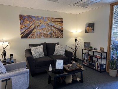 Therapy office with a couch and chair, a small shelf, and floor lamp