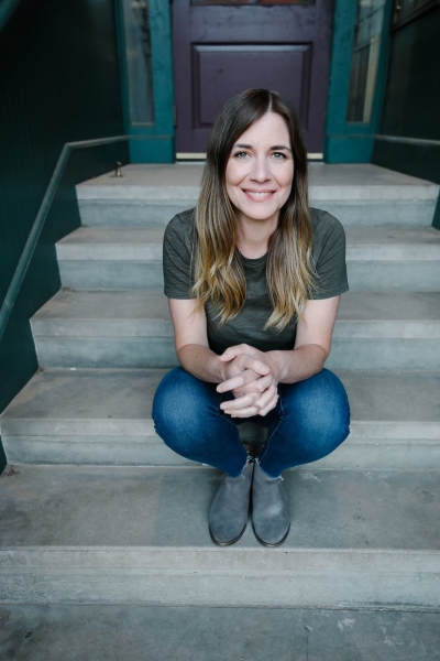 Sara Bryan, licensed professional counselor, smiling, sitting on concrete stairs, wearing jeans and an olive green T-shirt