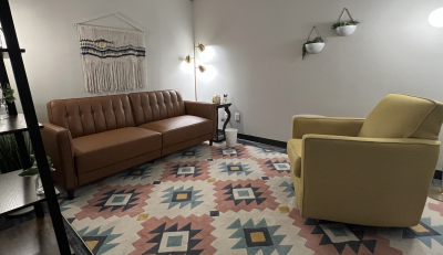 Therapy office with a couch and chair, area rug, and floor lamp.